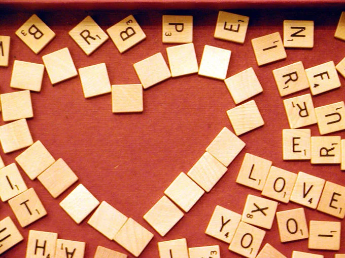 Hasbro — Scrabble tiles arranged in a heart shape on a red surface with LOVE spelled to the side