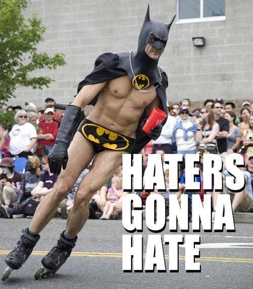 Man in Batman costume rollerblading in a parade with 'Haters gonna hate' caption