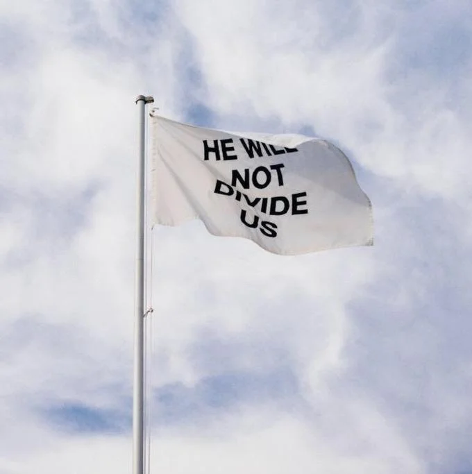 'He Will Not Divide Us' flag flapping on a flagpole in cloudy sky at an unknown location