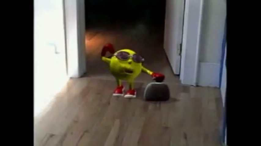 Here Comes Pacman — Yellow Pac-Man toy with sunglasses and red gloves standing in a hallway next to a small rock.