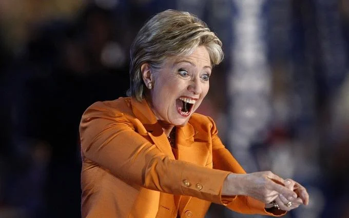 Hillary Clinton making an excited expression in orange pantsuit