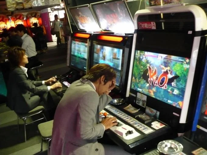 His Smile And Optimism: Gone — Man in suit slumped over arcade fighting game cabinet showing K.O. on screen.