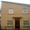 Hitler House — Straight-on photograph of the yellow-tan house with white windows and red door capturing unintentional facial features.