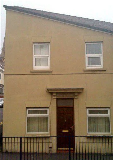 Hitler House — A yellow-tan colored residential house photographed straight-on with windows and red central door creating unintentional facial resemblance.