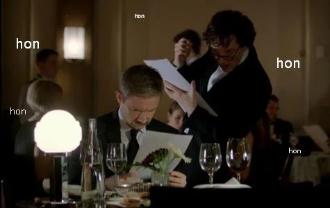 Hon Hon Hon — Film still showing people at dinner table with wine glasses and repeated 'hon' text labels pointing to different people.