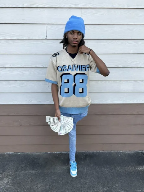 Hood Cryptids Withered Yns — Young man in blue beanie and Osavier 88 jersey posing with fanned cash outside a house