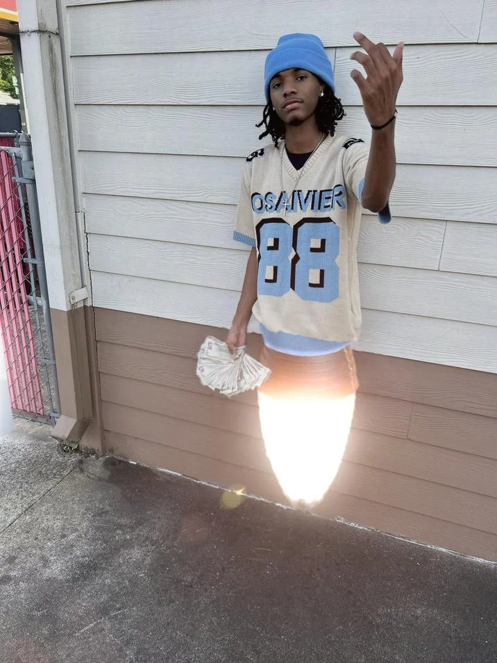 Hood Cryptids Withered Yns — Young man in blue beanie and Osavier 88 jersey holding fanned cash with lens flare