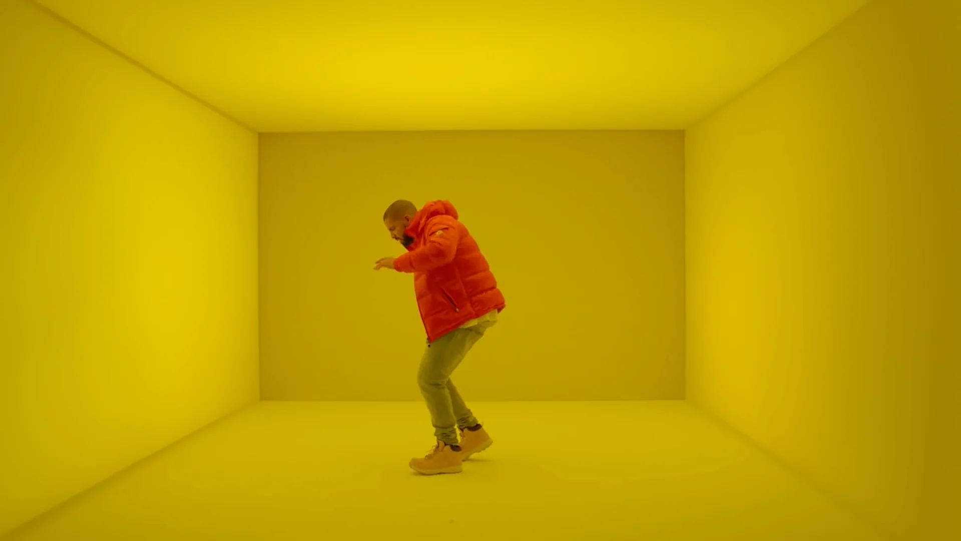 Drake dancing in a red puffer jacket inside a yellow-lit room in the Hotline Bling music video