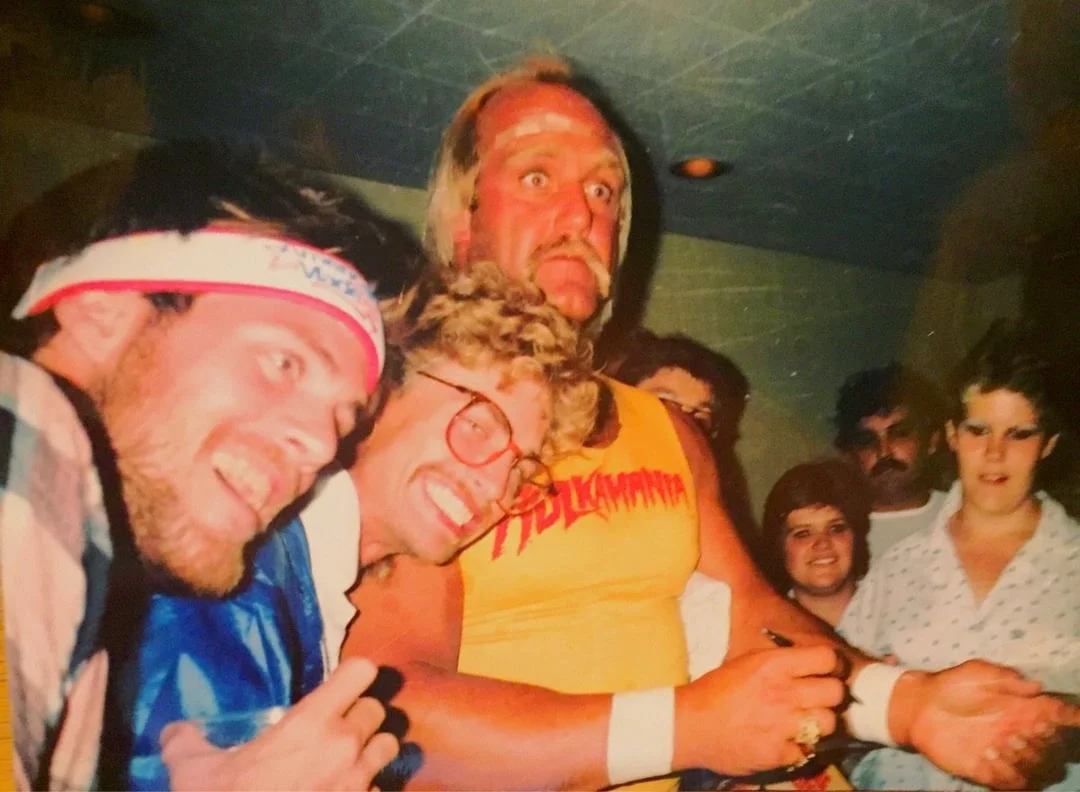 Hulk Hogan wearing a hard hat and white tank top on a construction site next to another worker
