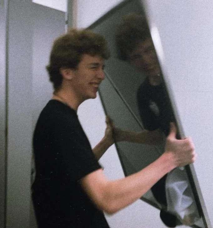 Hunter Schaffner and Holden Goyette Mirror Incident — Young man smiling while carrying a large mirror inside a bathroom