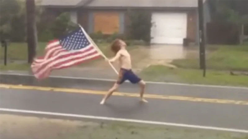 Hurricane Matthew Meets Slayer — Shirtless man with long hair running in torrential rain waving American flag during Hurricane Matthew.