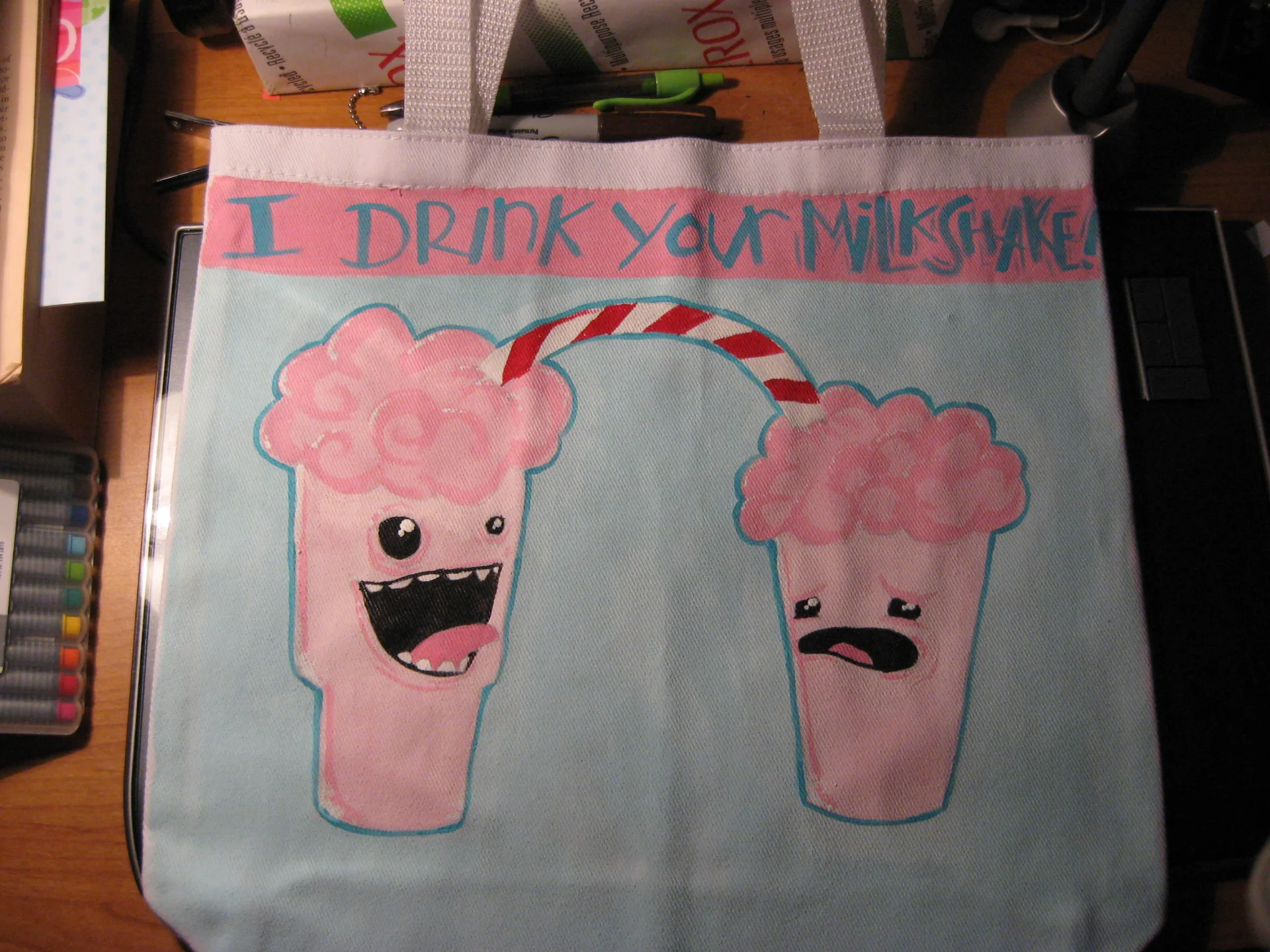 I Drink Your Milkshake! — Painted tote bag with two cartoon milkshake cups and the phrase 'I drink your milkshake'