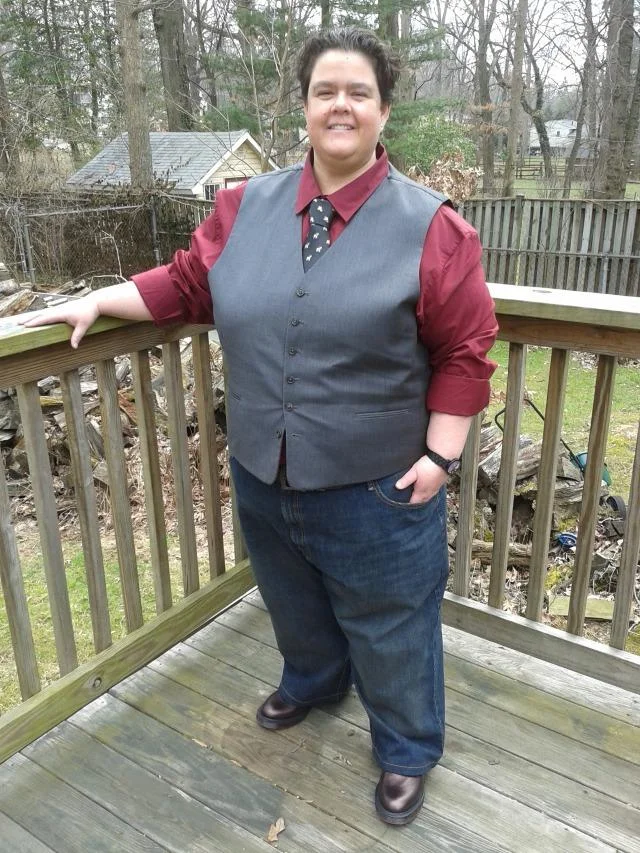 I Know She Be Running A McDonald's Like It's The Navy — Original photo of a person in a vest and tie posing on a wooden backyard deck.
