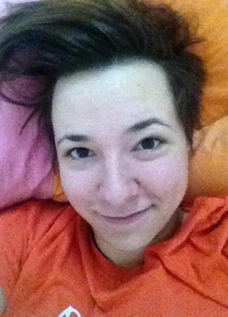 I Woke Up Like This — Woman with messy short hair on an orange pillow, taking a morning selfie.