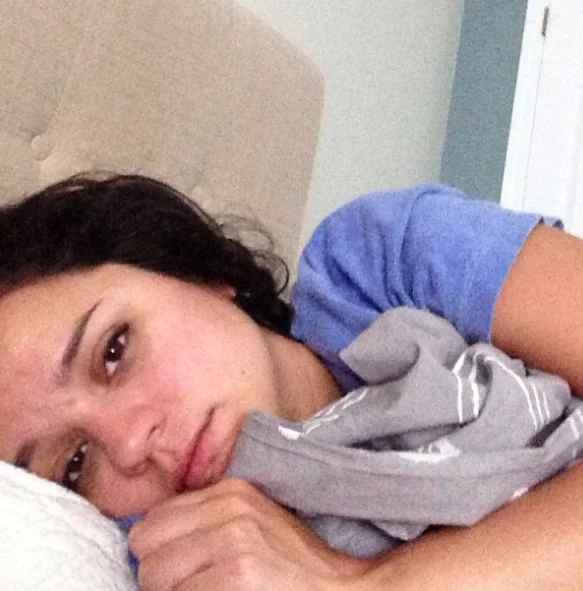 I Woke Up Like This — Tired woman in bed clutching a pillow, taking a groggy morning selfie.