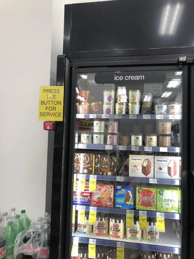 Ice Cream Challenge — Retail store glass-door ice cream freezer locked with bright yellow sign reading 'PRESS THE BUTTON FOR SERVICE'.