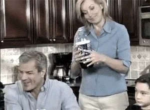 Infomercial Fails — Grainy GIF still showing woman struggling to close large shaker or blender container at kitchen counter.