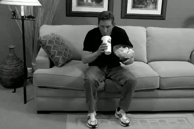 Infomercial Fails — Black-and-white still of man on couch awkwardly holding drink cup and snack bowl looking strained.