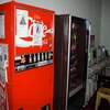 Internet Coke Machine — Red Coca-Cola vending machine standing in hallway alongside other vending machines in office or university environment.