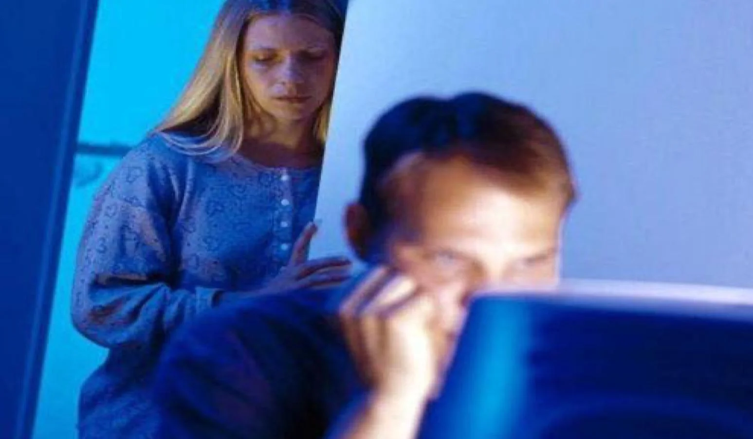 Internet Husband — Man engrossed in glowing computer screen at night with wife standing behind him in blue nightgown looking sad