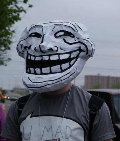 Internet Is Leaking — Person wearing large paper troll face mask at outdoor event with 'U MAD' text on shirt.