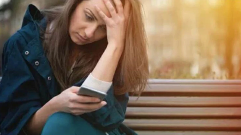Is Your Child Texting About — Worried woman sitting on a bench holding a phone with head in hand