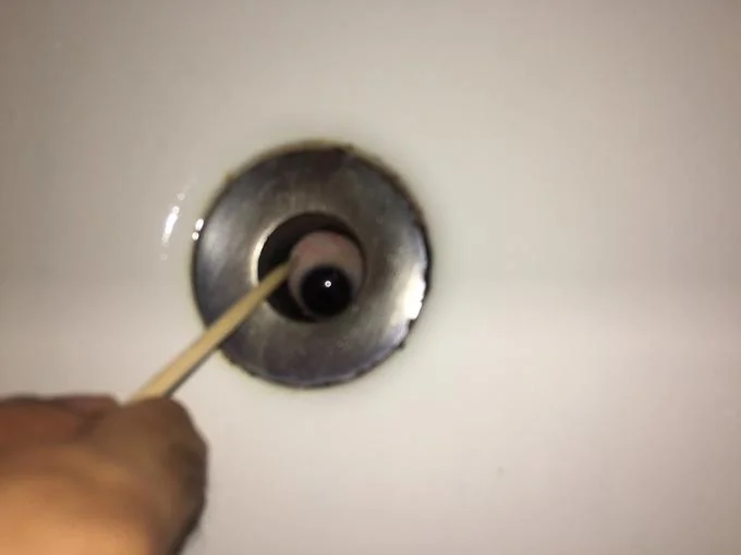 It Lives In My Sink — Blurry image of a hand with a stick probing an eye inside a sink drain
