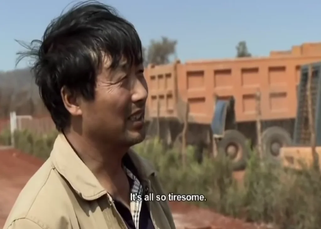 Chinese man in beige jacket on dirt road with subtitle 'It's all so tiresome.'