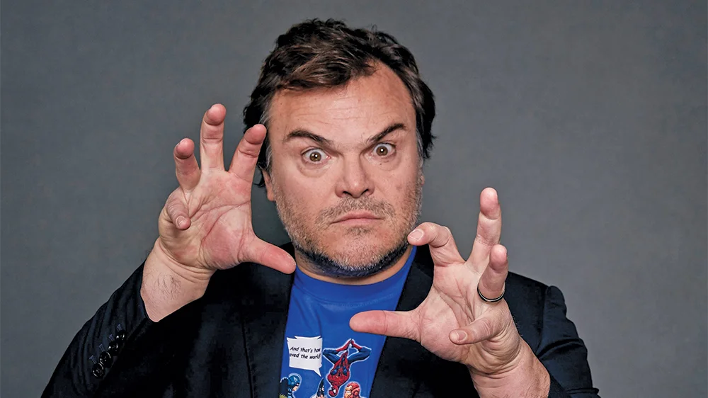 Jack Black making a wide-eyed expression with his hands raised in claw poses against a gray background