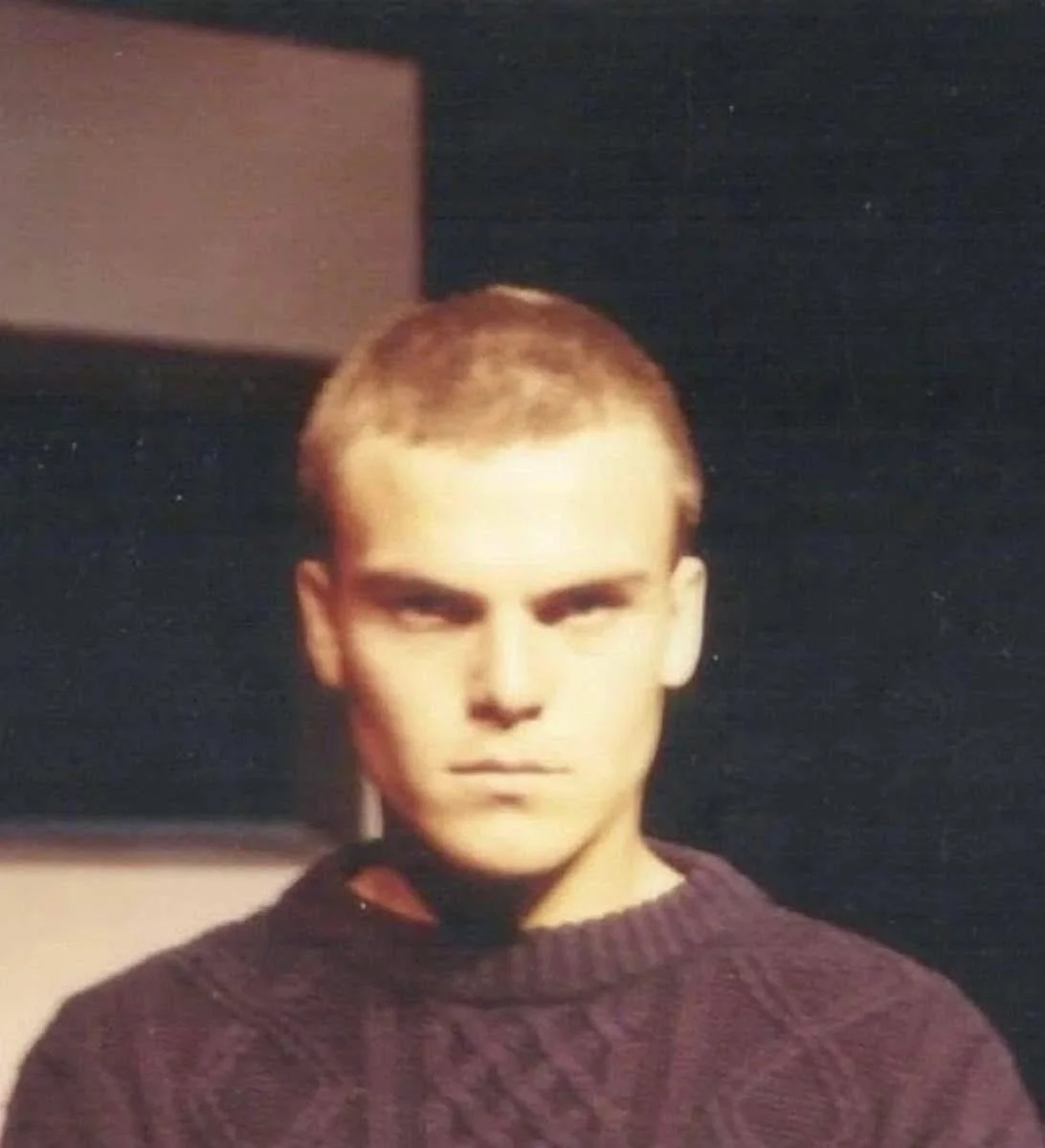 Vintage photo of a young Jack Black with a buzz cut and serious expression, wearing a purple knit sweater