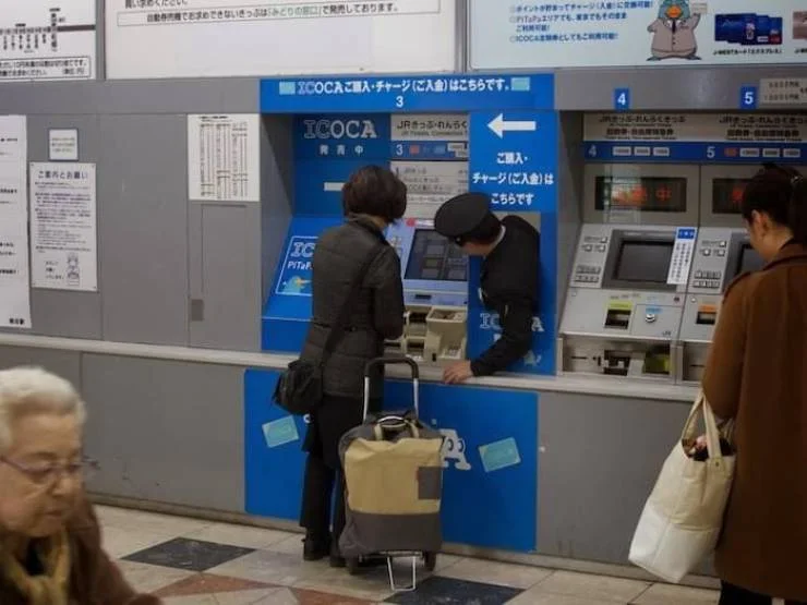 Japanese train station attendant helping a passenger at an ICOCA ticket machine