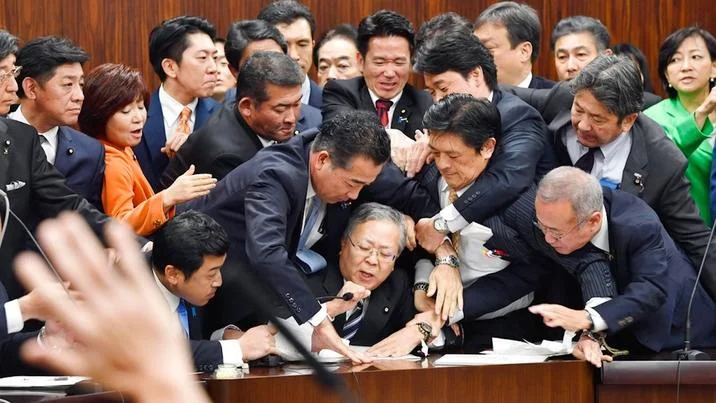 Japanese Parliament Trying To Stop Shinichi Yokoyama — Wider view of Japanese politicians restraining Yokoyama with a hand raised in protest in the foreground