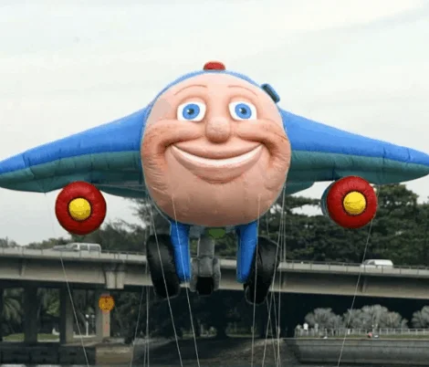 Animated GIF of a giant Jay Jay the Jet Plane parade balloon flying over a road
