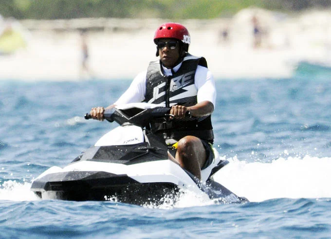 Jay-Z On a Jet-ski — Jay-Z riding a jet ski with a beach and swimmers visible in the background