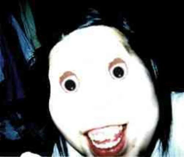 Close-up portrait of Jeff the Killer with pale white skin, black rings around hollow eyes, and a wide unsettling red mouth revealing teeth.