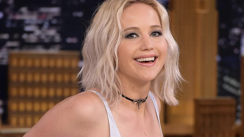 Jennifer Lawrence smiling with blonde bob hair on a talk show set