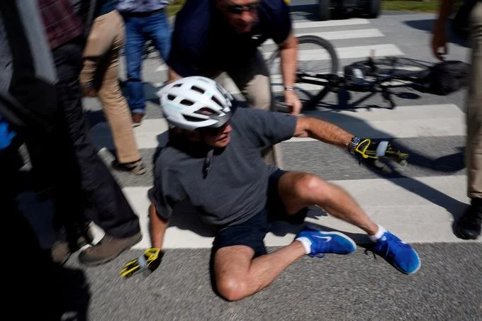 Joe Biden Falls Off Bike — Joe Biden on the ground after falling from his bike as aides rush to assist him.