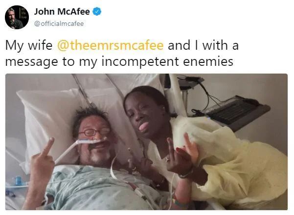 John McAfee and wife giving middle fingers in hospital bed