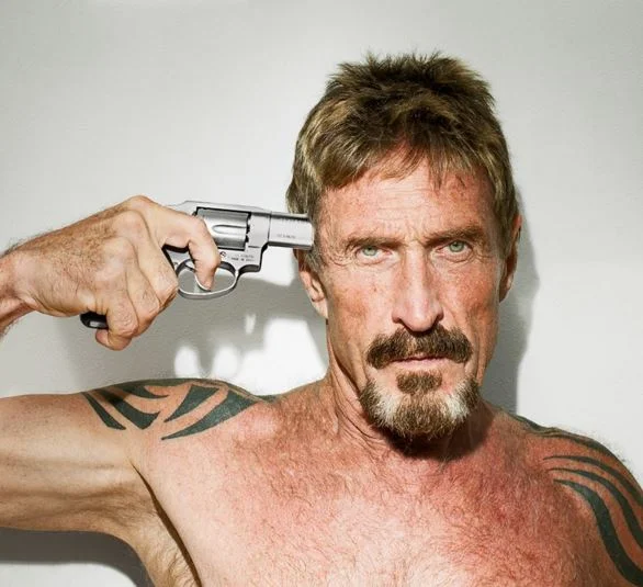 Shirtless John McAfee holding a revolver to his head