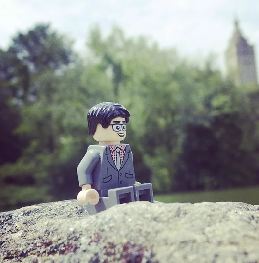 LEGO minifigure of John Oliver in a suit and glasses posed outdoors