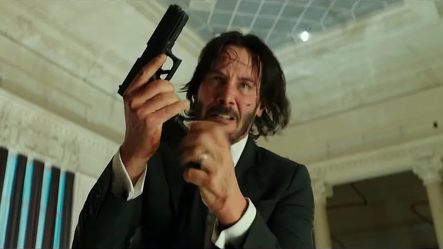 John Wick Reloading — John Wick holding a pistol upright while reloading, angry expression, bloodied face