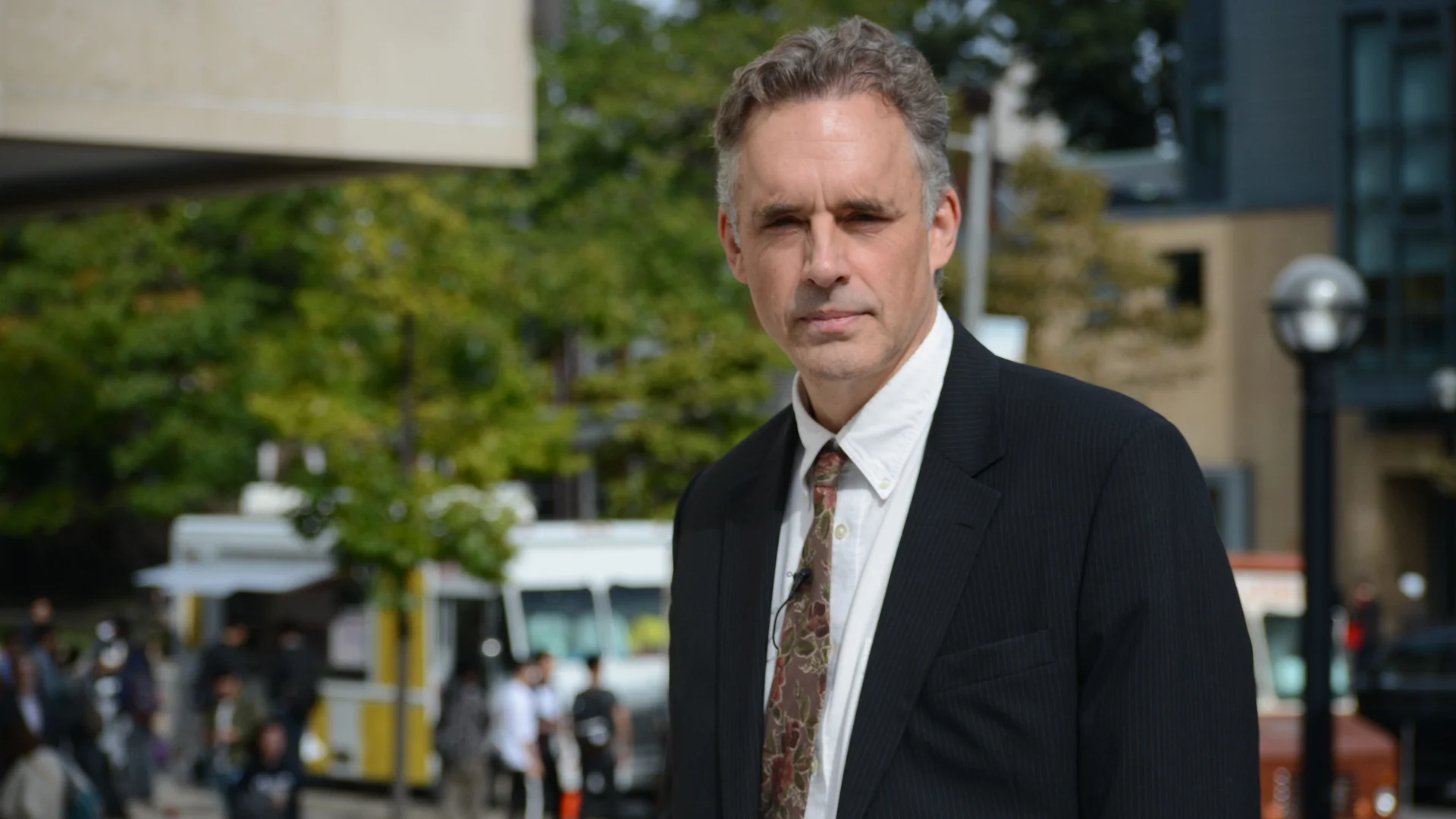 Jordan Peterson in a dark suit and floral tie standing outdoors in a city setting