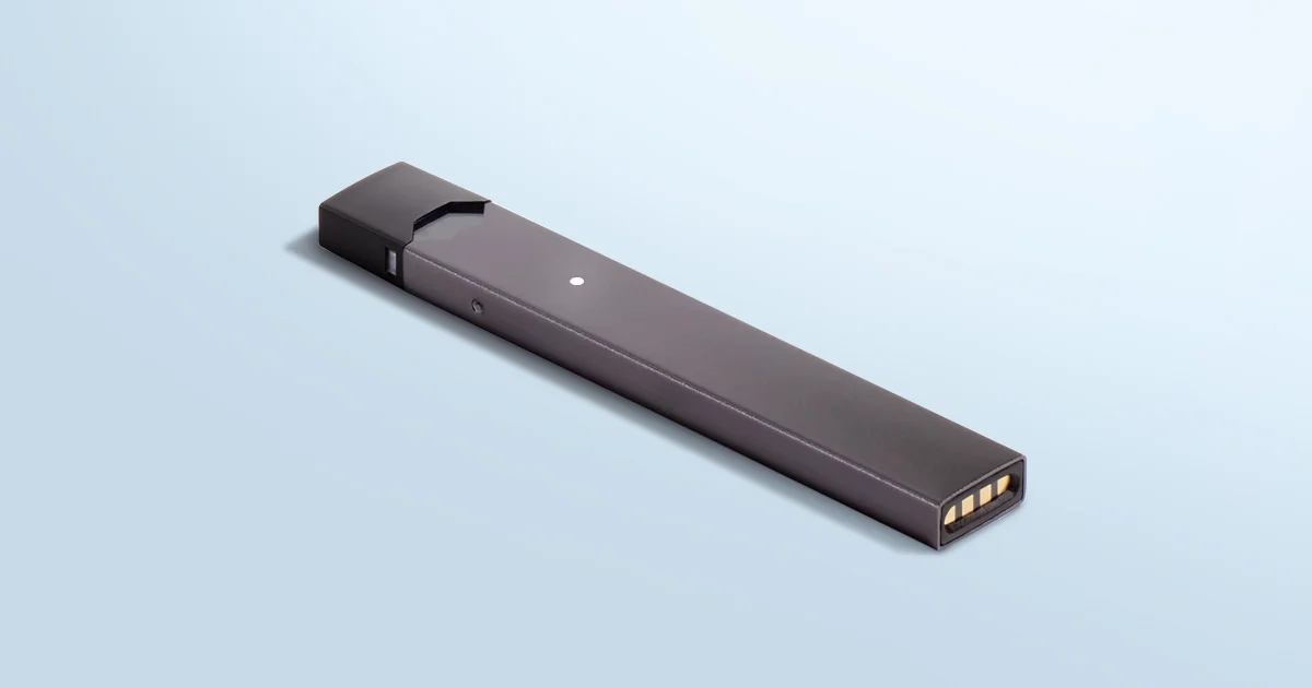 Dark gray JUUL vape device lying on light blue background