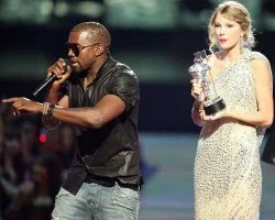 Kanye Interrupting — Kanye West on stage at the 2009 MTV Video Music Awards in white and gold blazer holding microphone with Taylor Swift beside him in white