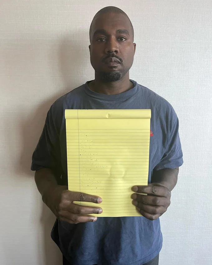 Kanye West Holding Notepad — Kanye West in same pose as original holding yellow legal pad with blank or barely visible text for editing.