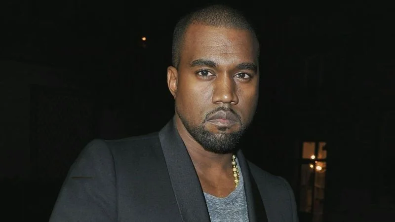 Kanye West in a dark blazer and gray shirt with gold chain necklace