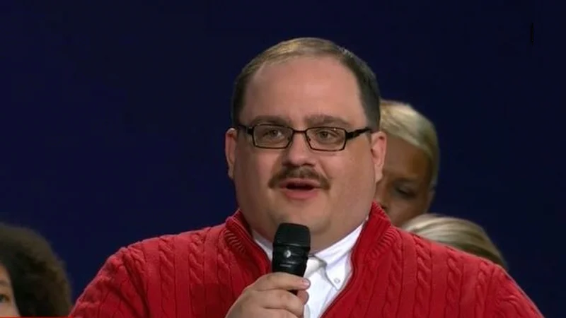 Ken Bone in a red sweater and glasses speaking into a microphone at the presidential debate