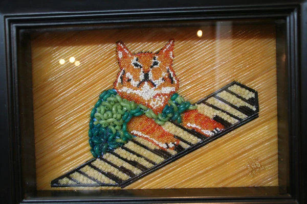 Keyboard Cat — Framed mosaic beadwork showing orange cat in green shirt with paws on keyboard in wooden-toned frame.