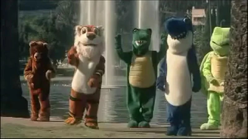 Lalalalalalalalalala — Five colorful animal mascot characters stand in a line dancing together, including a brown bear, tan mascot, green alligator, blue