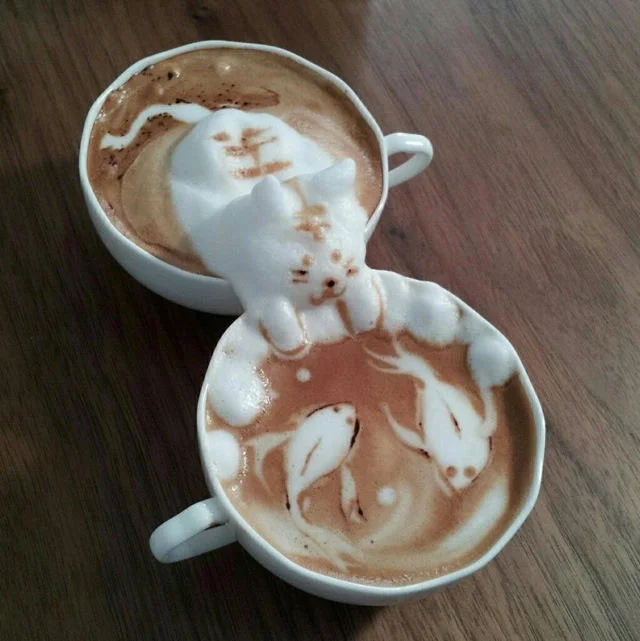 Latte Art — Two cappuccino cups with 3D milk foam sculpture of a cat and koi fish designs.